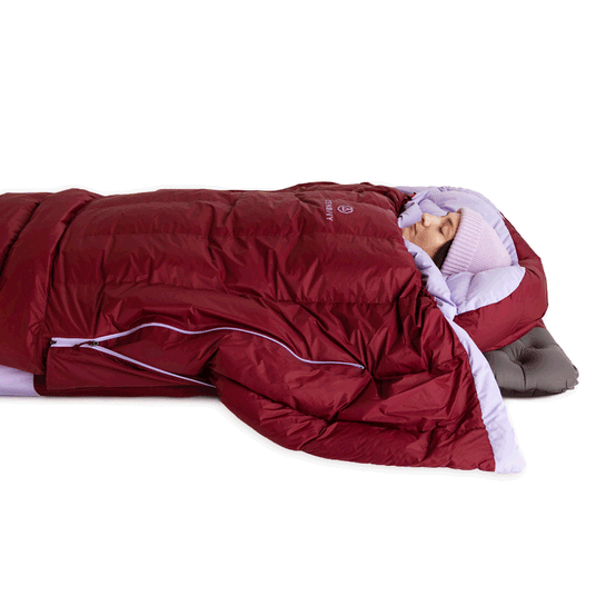 Camper sleeping inside a red Zenbivy quilt system, demonstrating how the design blocks drafts around neck and shoulders.