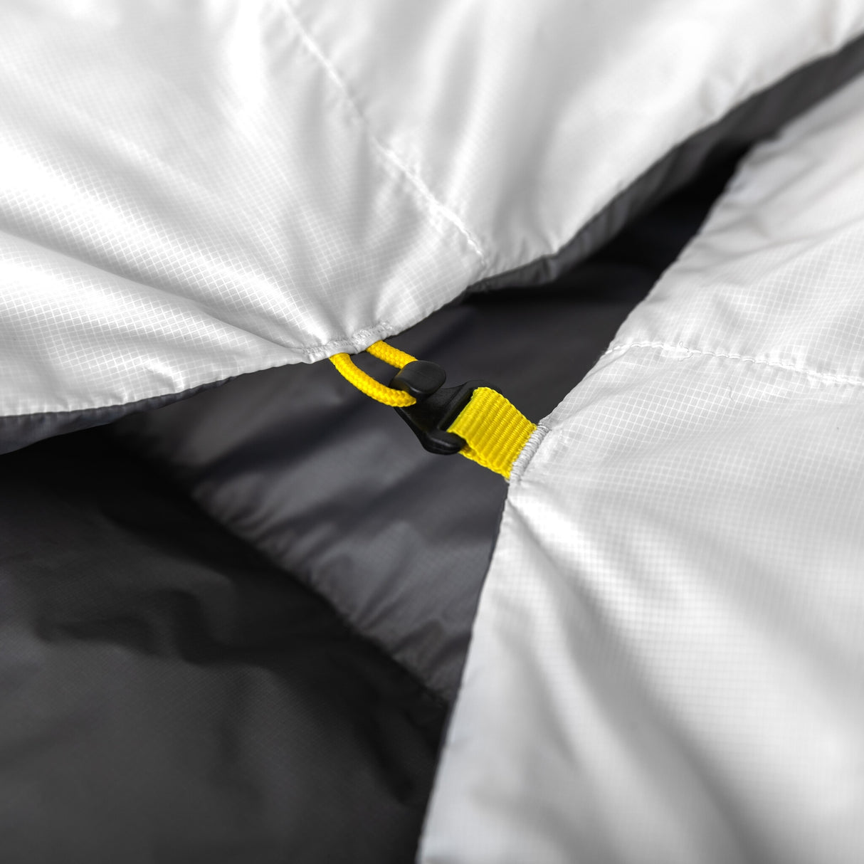 Detail of Zenbivy quilt clip system with yellow strap, securing the quilt to sheet for a draft-free, modular backpacking sleep setup.
