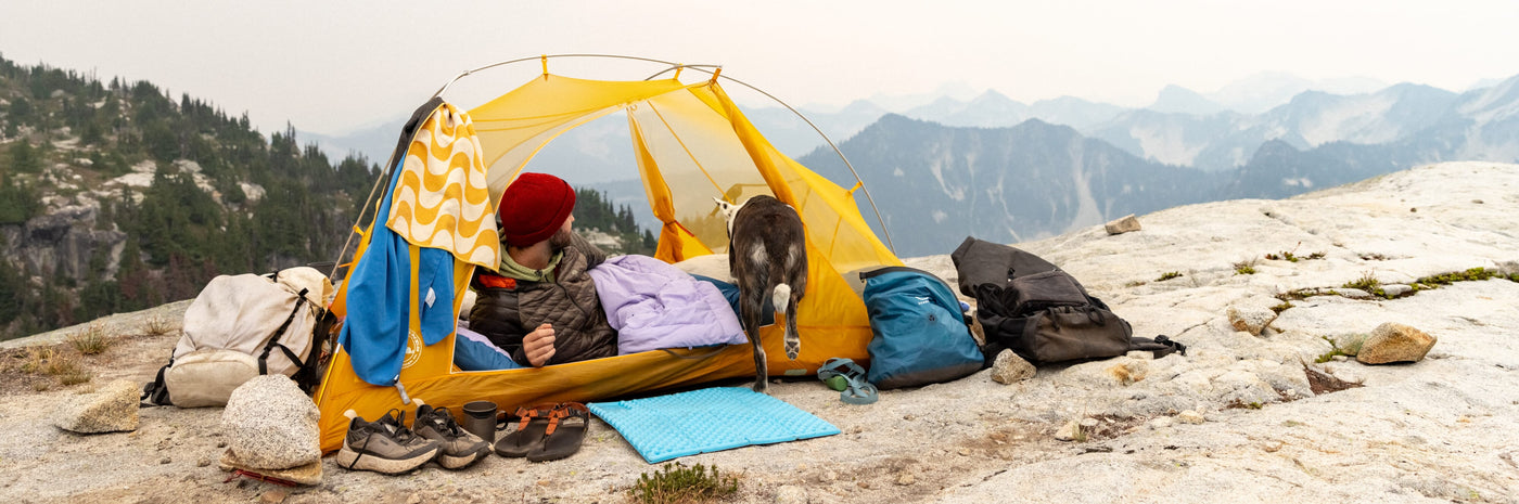 Person camping in a yellow tent with mountains in the background