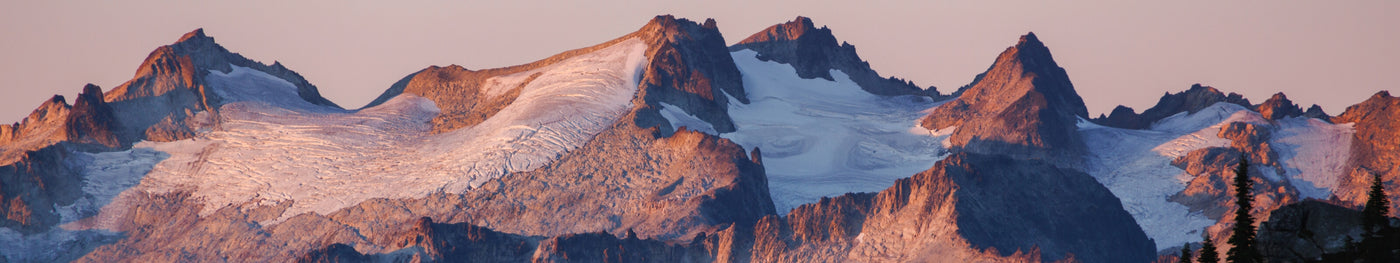 Sunlit alpine peaks with glacier and rugged rocky ridges at sunset, showcasing remote mountain wilderness.