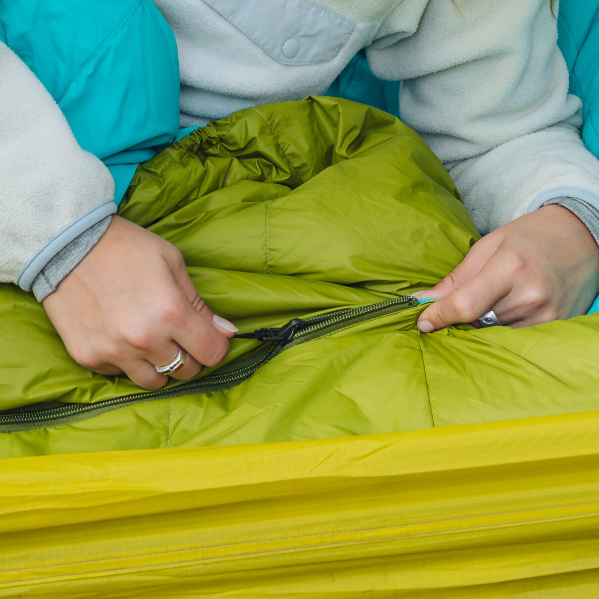 Close-up of hands zipping a green Zenbivy quilt, demonstrating the zipper closure system.