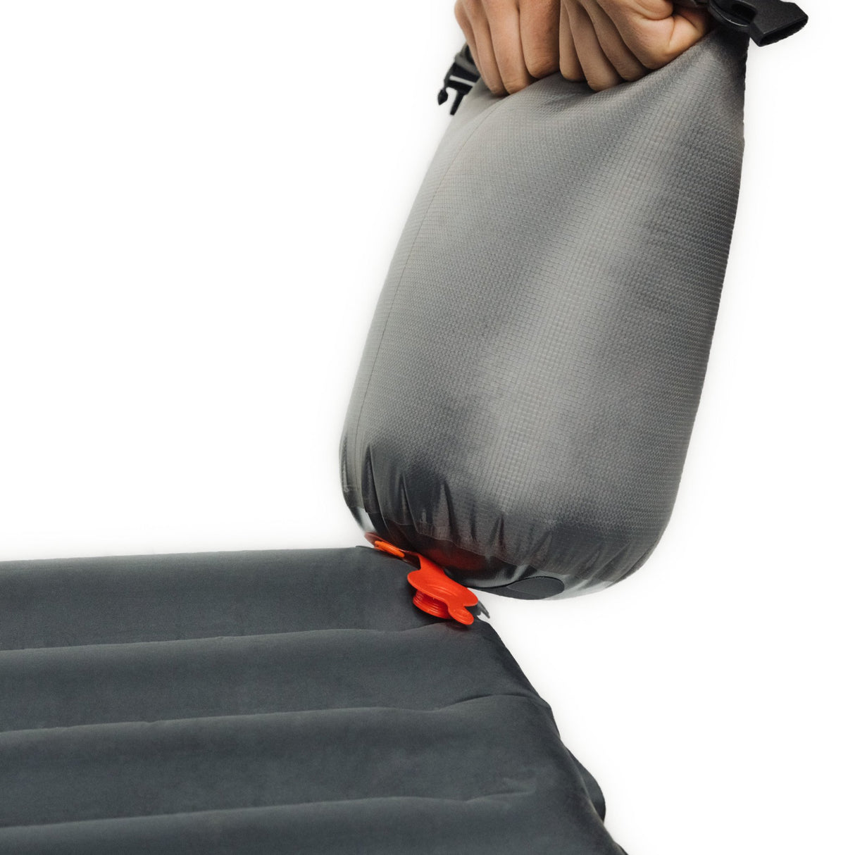 A hand holding a gray Zenbivy inflation sack, connected to a black inflatable sleeping pad via a valve.
