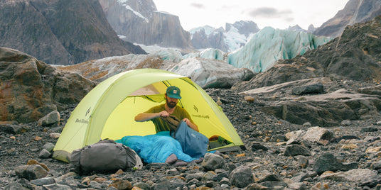Person unpacking their Zenbivy Pack Liner in a yellow tent in a rocky area with a glacier in the background.