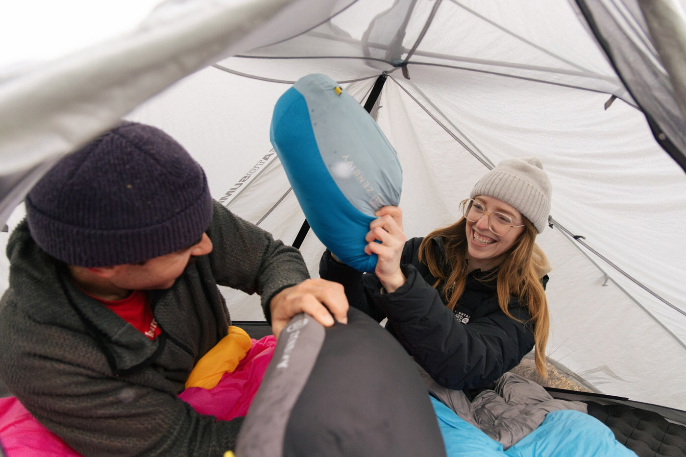 Two people inside a tent with pillows, one person holding a blue pillow and pretending to have a pillow fight with the other.