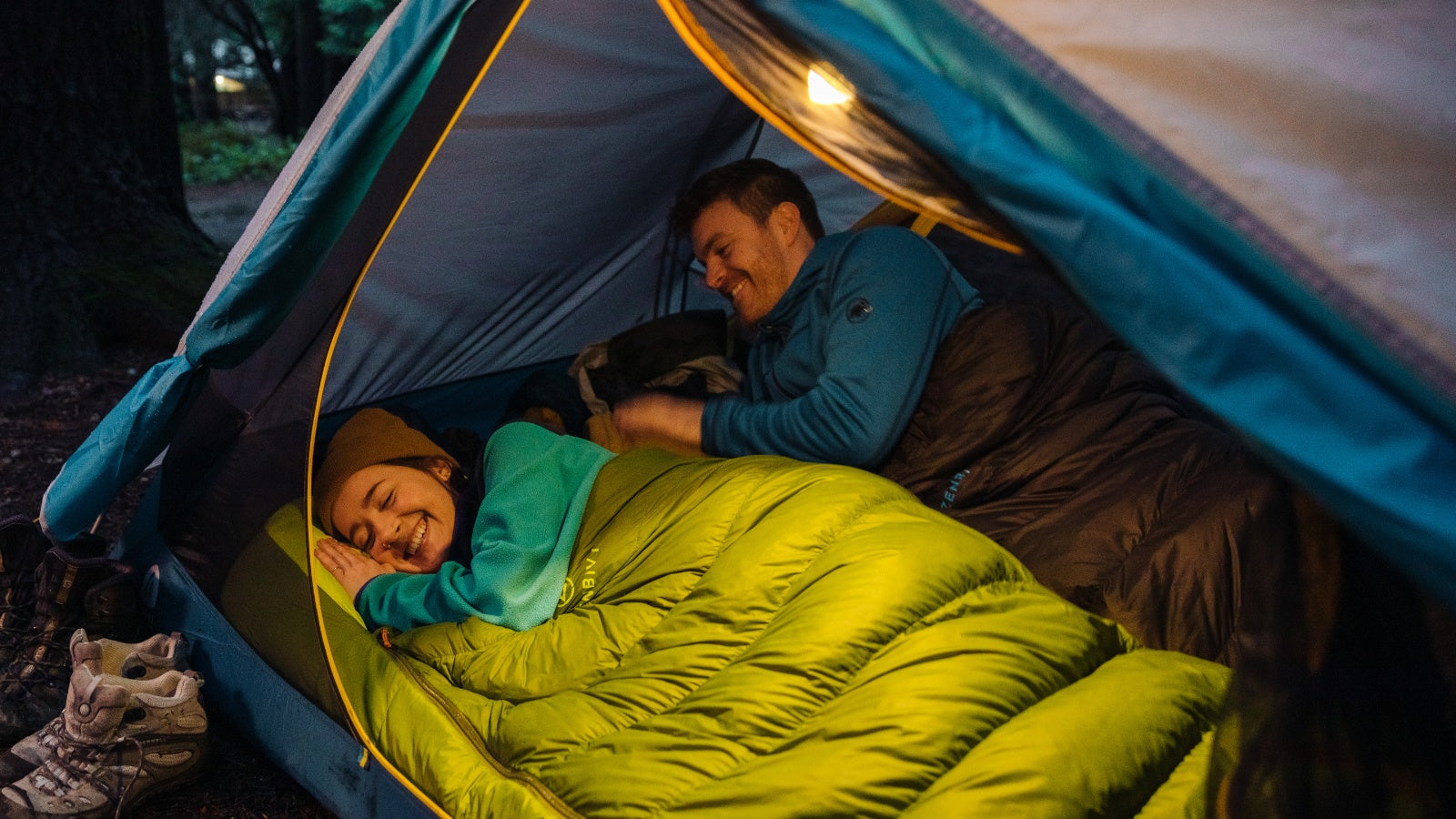 Camping couple tucked into their Zenbivy Bed sleeping bags inside their tent