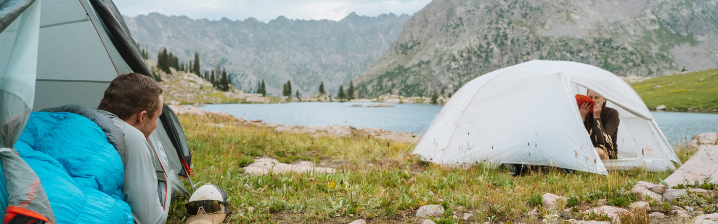 Person laying in one tent looking out the tent door towards their friend who is in another tent nearby